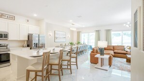 Une cuisine moderne avec des meubles blancs, un îlot central doté de tabourets et un coin repas avec une longue table et des chaises.