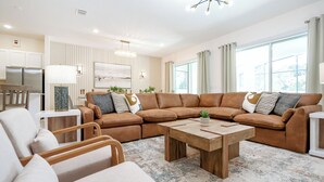 Un salon moderne avec un canapé d’angle marron, une table basse en bois et une grande fenêtre agrémentée de rideaux.
