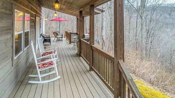 Eine Holzterrasse mit Schaukelstühlen und einem Tisch mit Blick auf ein bewaldetes Gebiet.