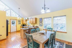 A spacious kitchen with wooden cabinets, a dining table with chairs, and large windows allowing natural light. - Outstanding mountain home with firepit, fast WiFi, furnished deck, views & grill (Sylva)