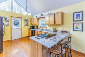 A kitchen with wooden cabinets, a marble countertop, and a built-in island with bar stools. - Outstanding mountain home with firepit, fast WiFi, furnished deck, views & grill (Sylva)