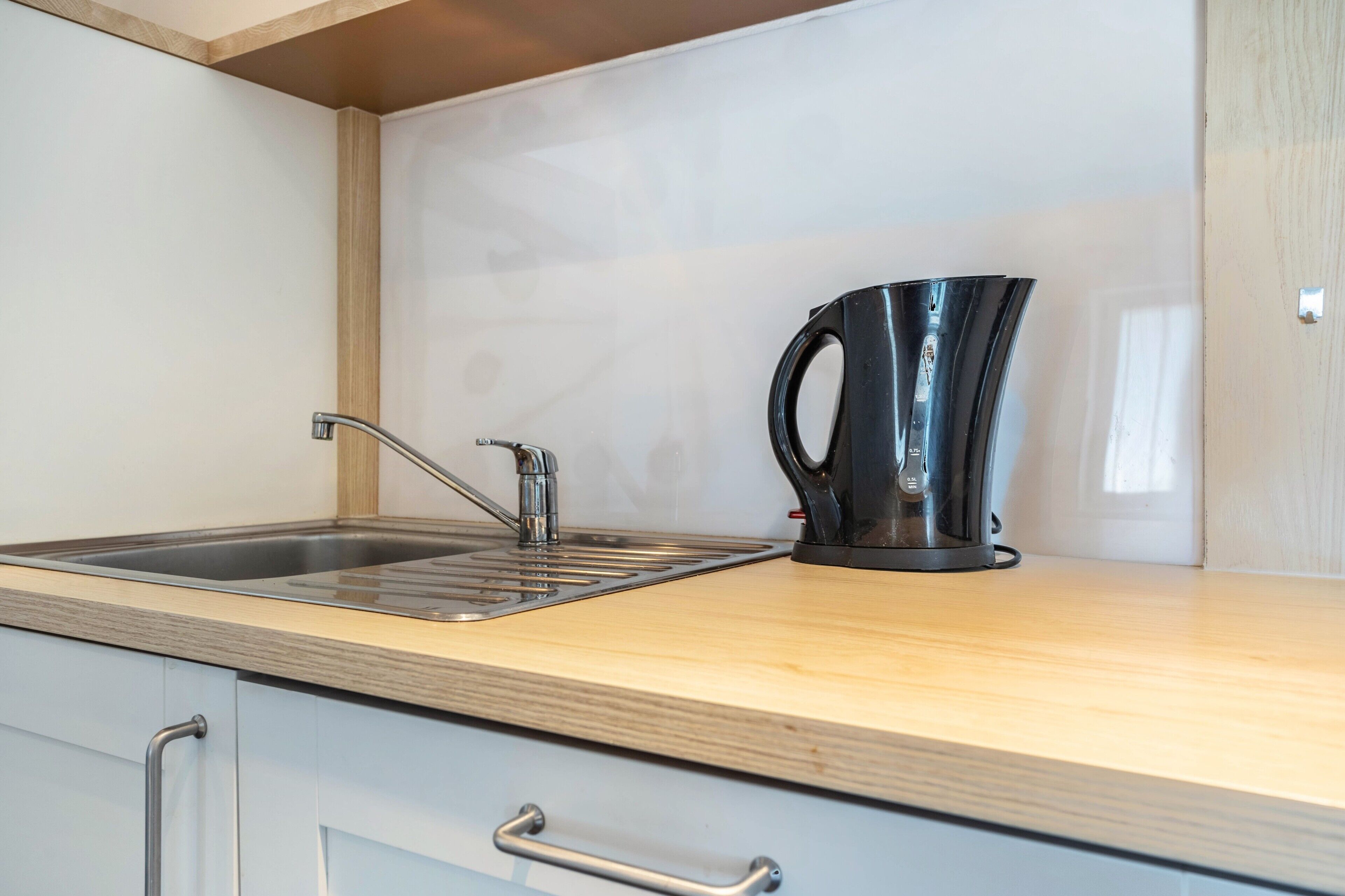 A kitchen with a stainless steel sink, a black kettle, and wooden countertops.