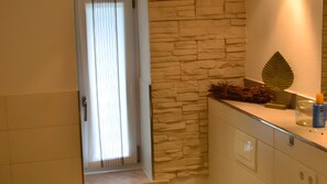 A bathroom with a stone wall, a mirror, and a door leading to another room. - Holiday Home for Up to 6 Guests (70 m²) in Trent (Rügen) (Trent)