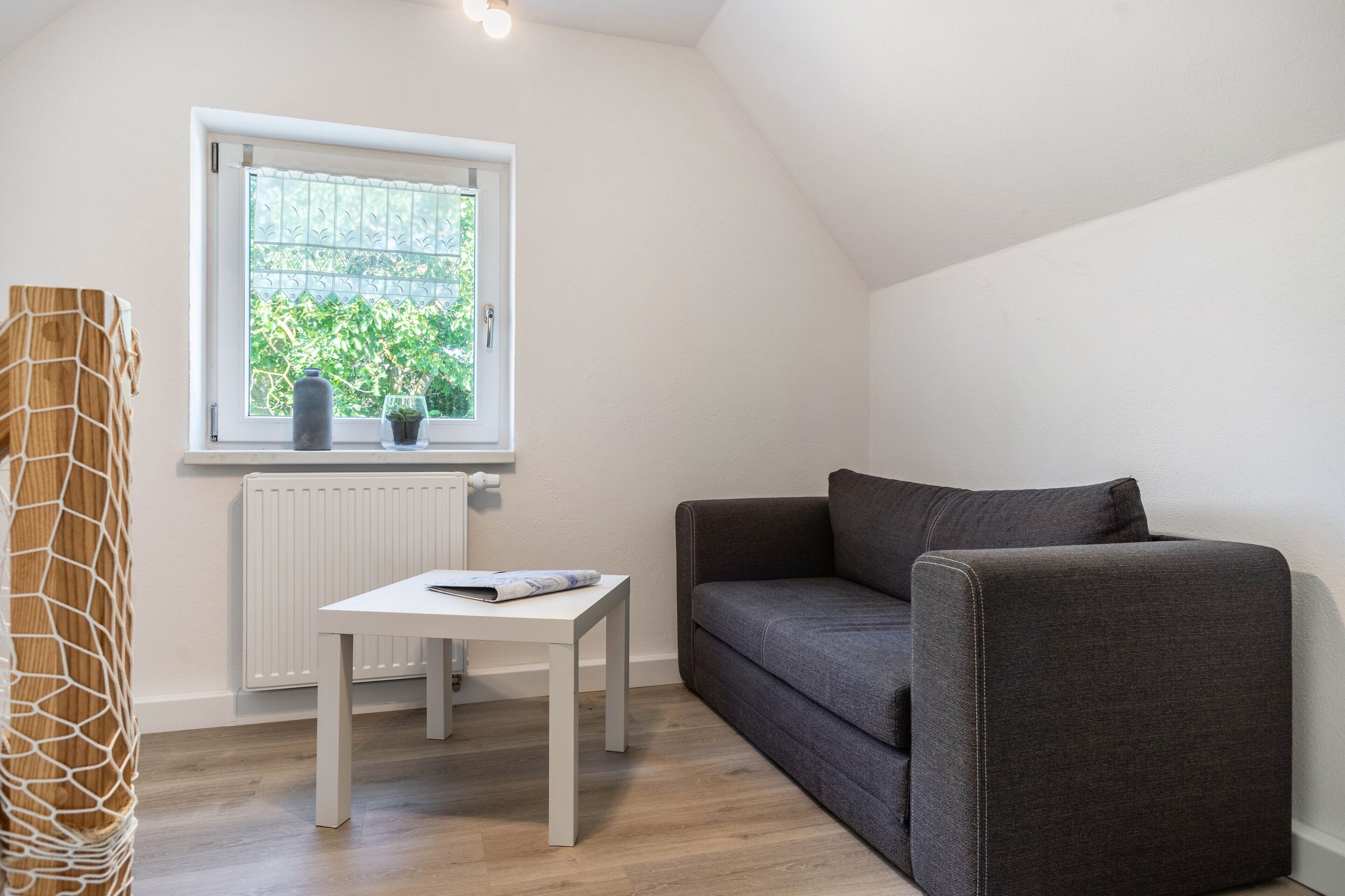 A room with a window, a white radiator, a grey sofa, and a white table.