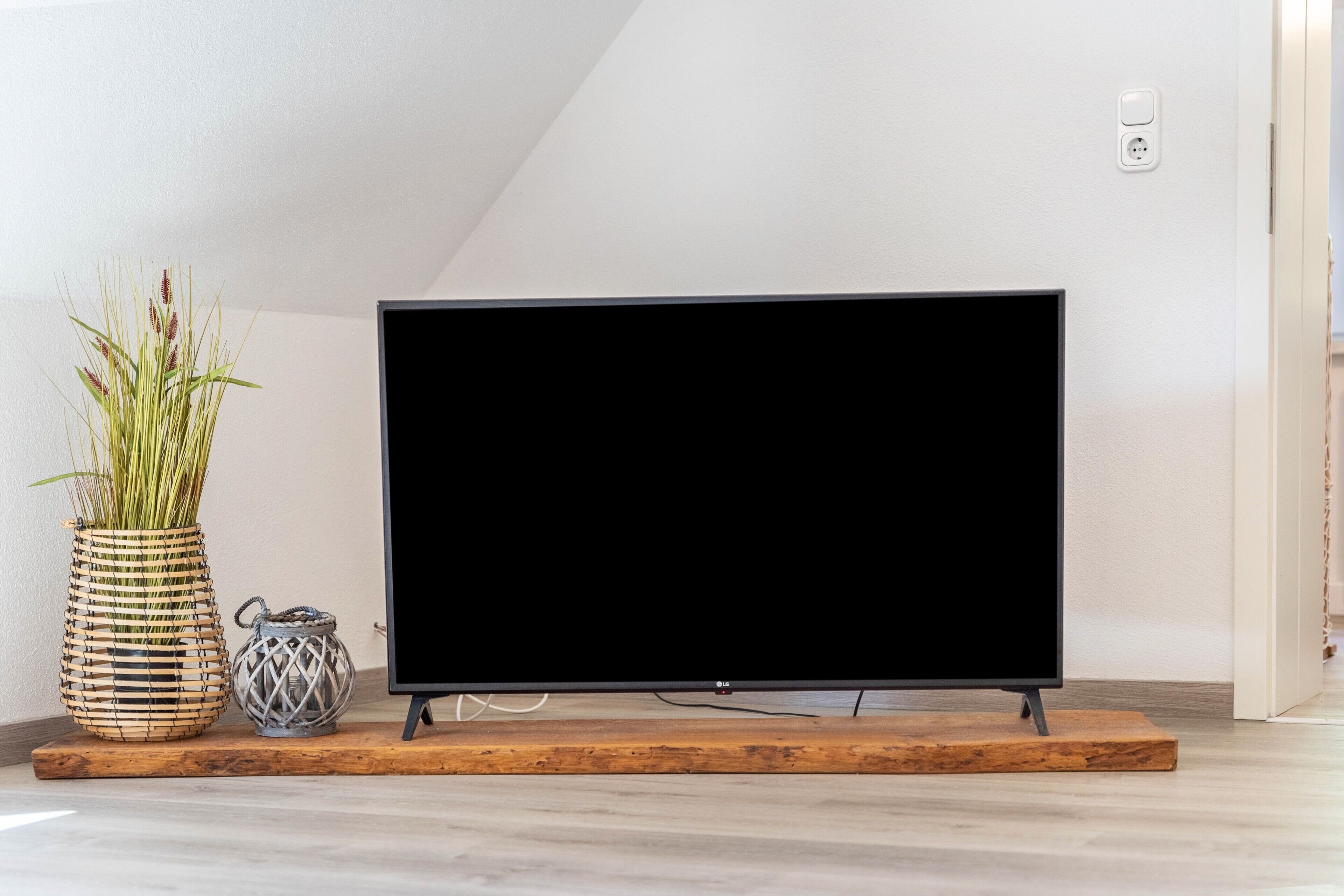 Un téléviseur à écran plat, posé sur un meuble en bois, dans une pièce aux murs blancs et au plancher en bois.