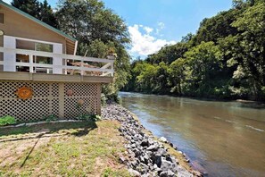 A riverside building with a balcony, a wooden fence, and a rocky riverbank. - Country Cottage (Sylva)