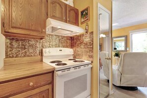 A kitchen with wooden cabinets, a white stove, and a beige chair. - Country Cottage (Sylva)