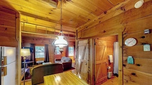 Interno di una baita di legno con un tavolo da pranzo, sedie, una lampada, una sveglia e una porta.