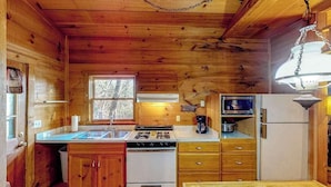 Una cucina compatta con pareti in legno, un fornello, forno, frigorifero e una finestra.