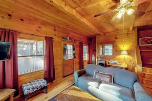 A cabin interior with wooden walls, a sofa, a bench, a television, and a ceiling fan. - Comfortable mountain view cabin with TV, board games, & kitchenette (Scaly Mountain)