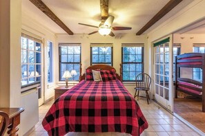 Une chambre à coucher avec un lit, une chaise, un ventilateur de plafond et de grandes fenêtres.