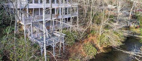 A treehouse with multiple levels and a staircase, surrounded by dense trees and a small stream.