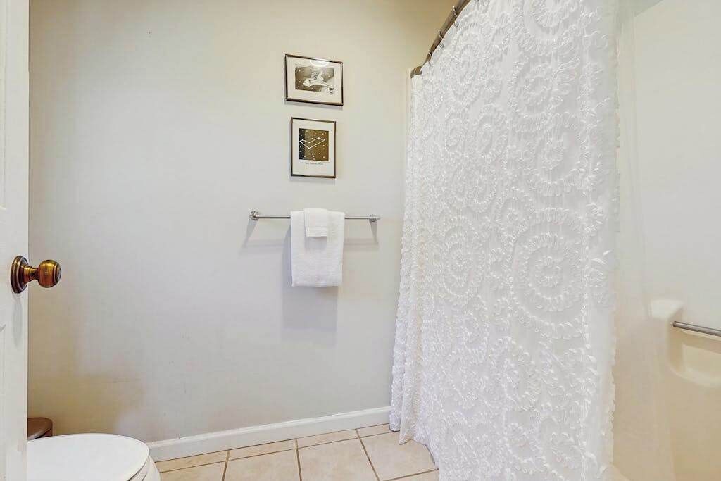 A bathroom with a white toilet, a towel rack with a white towel, and a shower curtain.