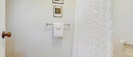 A bathroom with a white toilet, a towel rack with a white towel, and a shower curtain.