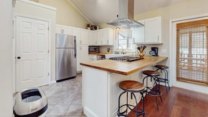 A kitchen with white cabinets, a stainless steel refrigerator, a wooden island with stools, and a window with blinds. - Ripple Run (Sylva)