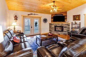 Ein Wohnzimmer mit Ledersofas, Kamin, Flachbildfernseher und Deckenventilator.