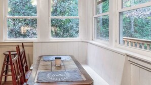 Ein Zimmer mit einer hölzernen Sitzbank, einem Tisch mit Kerze und großen Fenstern mit Blick auf Bäume.