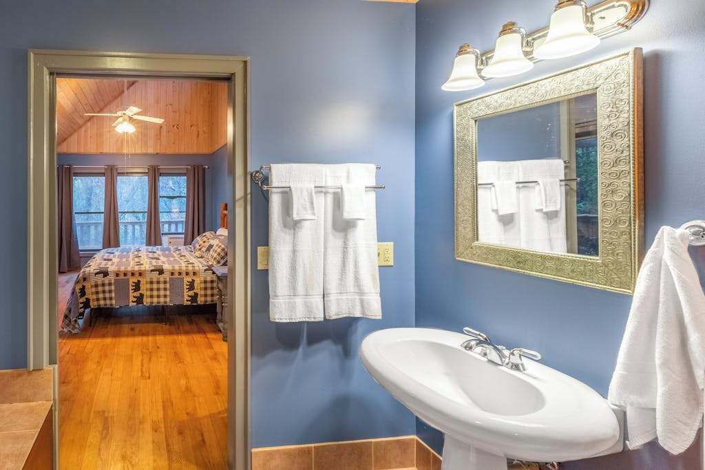 Une chambre avec un lit, une salle de bain avec un lavabo et un miroir, et un couloir menant à un balcon.