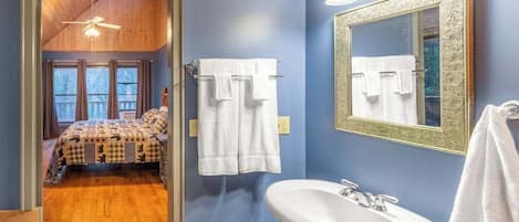 Une chambre avec un lit, une salle de bain avec un lavabo et un miroir, et un couloir menant à un balcon.