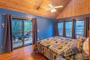 Une chambre à coucher avec un lit, un ventilateur de plafond et une vue sur l’extérieur grâce à de grandes fenêtres.