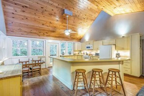 Une cuisine avec un plafond en bois, un îlot central doté de tabourets et des armoires blanches.