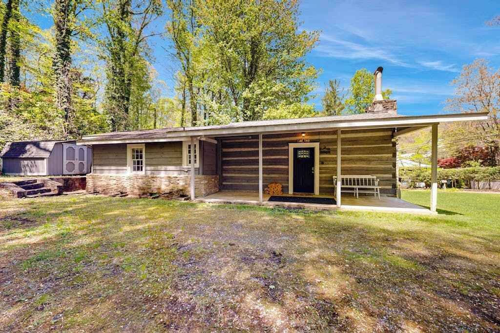 A log cabin with a porch, a chimney, and a small attached structure.