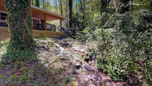 A cabin with a wooden deck, surrounded by dense forest.