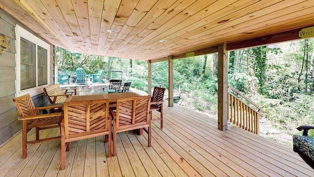 A wooden deck with a table and chairs, surrounded by a wooden railing and a view of a forest.
