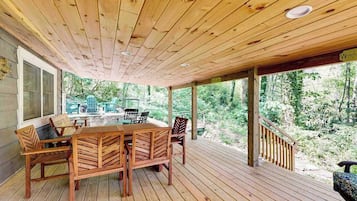 Une terrasse en bois avec une table et des chaises, entourée d’une balustrade en bois et offrant une vue sur une forêt.