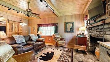 L’intérieur chaleureux d’un chalet avec un canapé en cuir, une cheminée en pierre et un téléviseur fixé au mur.