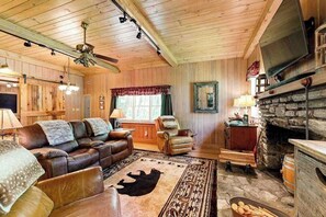 Ein gemütliches Blockhaus-Interieur mit Ledersofa, Kamin aus Stein und einem an der Wand befestigten Fernseher.