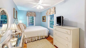 Ein Schlafzimmer mit Bett, Schminktisch, Deckenventilator und Fenstern.
