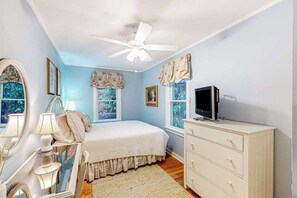 A bedroom with a bed, dresser, ceiling fan, and windows. - The Cottage on Chowan (Highlands)