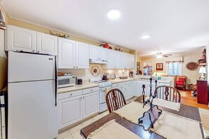 A kitchen with white cabinets, a refrigerator, stove, microwave, and dining table with chairs. - The Cottage on Chowan (Highlands)