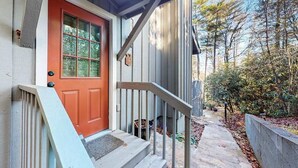 Ein Haus mit roter Tür, einer Holztreppe und einem steinigen Weg, der zu einem Garten führt.