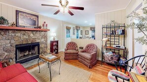 Ein gemütliches Wohnzimmer mit Kamin aus Stein, Deckenventilator und Bücherregal.