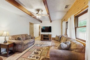 A living room with two sofas, a TV, wooden beams, a ceiling fan, and a window with curtains. - Hollow's End (Whittier)