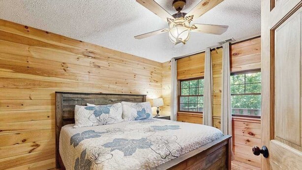 Ein Schlafzimmer mit Holzwänden, einem Bett, einem Deckenventilator und einem Fenster.