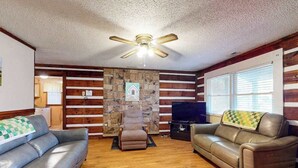 A living room with a stone wall, two leather sofas, a recliner, a TV, and a ceiling fan. - Family Jewel (Whittier)