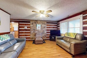 Ein Wohnzimmer mit Steinwand, zwei Ledersofas, einem Sessel, einem Fernseher und einem Deckenventilator.