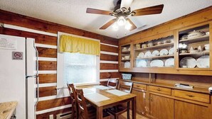 A wooden-paneled room with a dining table, chairs, a ceiling fan, and a cabinet with dishes. - Family Jewel (Whittier)