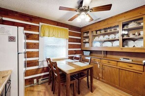 Ein Zimmer mit Holzwänden, einem Esstisch, Stühlen, einem Deckenventilator und einem Schrank mit Geschirr.