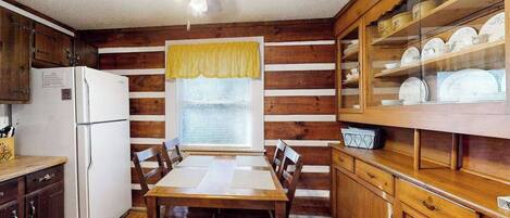 A kitchen with wooden cabinets, a dining table, chairs, a refrigerator, and a ceiling fan.