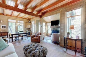 A spacious living room with a high ceiling, wooden beams, a fireplace, a television, and a dining area with a table and chairs. - Chic Highland Cabin (Highlands)