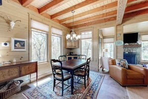 A wooden cabin interior with a dining table, chairs, a fireplace, and a leather sofa. - Chic Highland Cabin (Highlands)