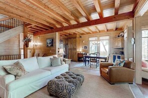 A spacious living area with a high wooden ceiling, a sofa, a chair, and a zebra-patterned ottoman. - Chic Highland Cabin (Highlands)