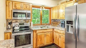 Una cocina con armarios de madera, un refrigerador de acero inoxidable, un microondas, un horno y una ventana con vistas a árboles.