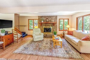 A living room with a fireplace, a sofa, a chair, a coffee table, and a TV. - Beautiful home with hot tub, firepit, deck, & central AC (Whittier)
