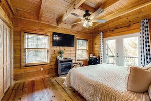 A wooden cabin bedroom with a bed, a ceiling fan, a TV, and a window. - Lost Indian Hideaway (Whittier)