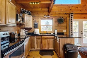 A kitchen with wooden cabinets, a black countertop, a sink, and a window. - Lost Indian Hideaway (Whittier)
